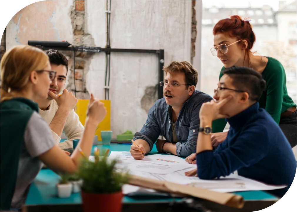 Cinco personas del equipo conversando alrededor de una mesa con planos
